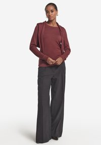 Felpa con cappuccio color amaranto con apertura frontale, maniche lunghe e vestibilità comoda. Abbinata a pantaloni neri a gamba larga e scarpe con tacco.