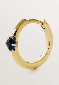 Pendiente de aro dorado que presenta una gema redonda de un azul intenso, engastada en un diseño de cuatro garras. La superficie es lisa con un acabado pulido.