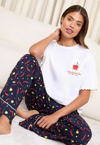 Tricou alb cu mânecă scurtă, cu margini ondulate și un print colorat. Pantaloni de pijama bleumarin, cu motive de ardei iute roșii și lime, cu accente verzi.