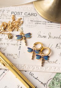 Zelta rotaslietu komplekts ar pūķa mušiņas kulonu un auskariem. Detalizēts zils un zelta emalja ar pērlīšu akcentiem. Ķēdes un riņķa dizaini.