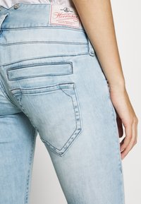Helle blaue Denim-Jeans mit hohem Bund, ausgestattet mit zwei Gesäßtaschen und einem roten Markenetikett, das auf der Rückseite gestickt ist.