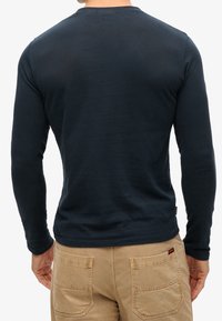 Marineblaues Langarmshirt mit Rundhalsausschnitt, schlichter Gestaltung, weicher Textur und leicht taillierter Silhouette. Getragen mit hellen Hosen.