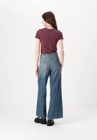 Donkerrode T-shirt met korte mouwen gecombineerd met hoge taille, wijde blauwe spijkerbroeken. Zwarte plateau schoenen maken de look compleet.