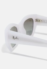 Ochelari de soare din plastic alb cu lentile gri, design unghiular ascuțit, accente metalice și un logo argintiu pe tâmplă.