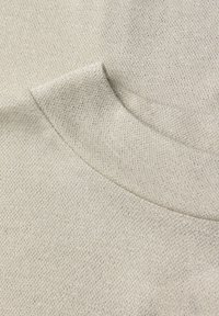 Světlý béžový pletený materiál s hladkou texturou. Má kulatý výstřih a jemný, nenápadný lesk. Bez viditelných vzorů nebo kovových doplňků.