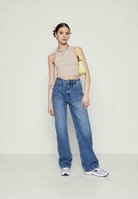Top cropped bege, jeans azuis de cintura alta e ténis brancos com acentos roxos. Bolsa verde e colar como detalhes notáveis.