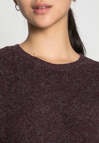 Stickad vinröd tröja med rund halsringning, texturerad tyg med mjuk känsla och en subtil fluffighet. Klassisk, mångsidig design.