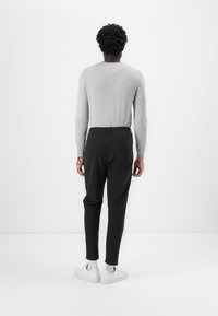 Haut à manches longues gris, pantalon noir à taille élastique et baskets blanches. Accent sur des lignes épurées, un design minimal et des couleurs neutres.