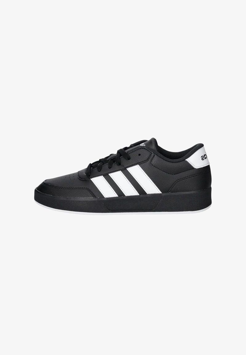 Zapatilla deportiva negra con una parte superior sintética lisa, que presenta tres rayas blancas, cordones redondos y una suela de goma plana.