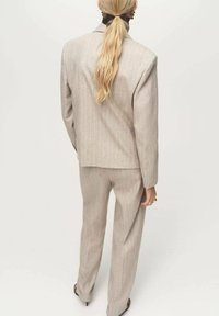 Traje gris claro a rayas con un blazer ajustado y pantalones rectos, fabricado en una tela texturizada. La vista posterior revela un diseño elegante.