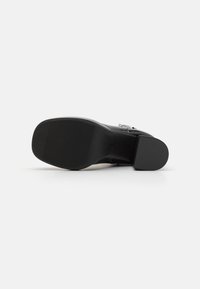 Zapato de tacón alto negro con parte superior de cuero liso, punta redondeada y suela de goma texturizada con ranuras horizontales para un mejor agarre.