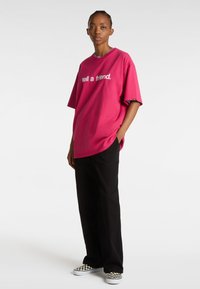Rosa oversized t-shirt med hvid tekst "fortæl en ven" og sorte vide bukser. Et par sort-hvide ternede slip-on sko.
