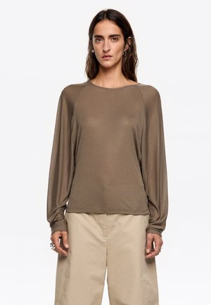 Brązowa bluzka z długim rękawem, uszyta z lekkiej tkaniny, z okrągłym dekoltem i luźnym krojem, w zestawieniu z beżowymi spodniami. Charakteryzuje się gładką teksturą i prostym designem.