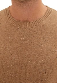 Nahaufnahme eines Mannes, der einen braun gesprenkelten Strickpullover mit geripptem Rundhalsausschnitt trägt.