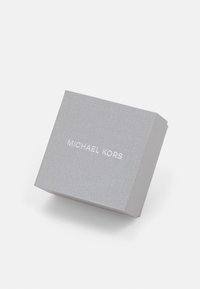 Hallitusseente tekstuuriga hall pappkast, mille peal on valget tooni reljeefselt graveeritud logo "MICHAEL KORS".