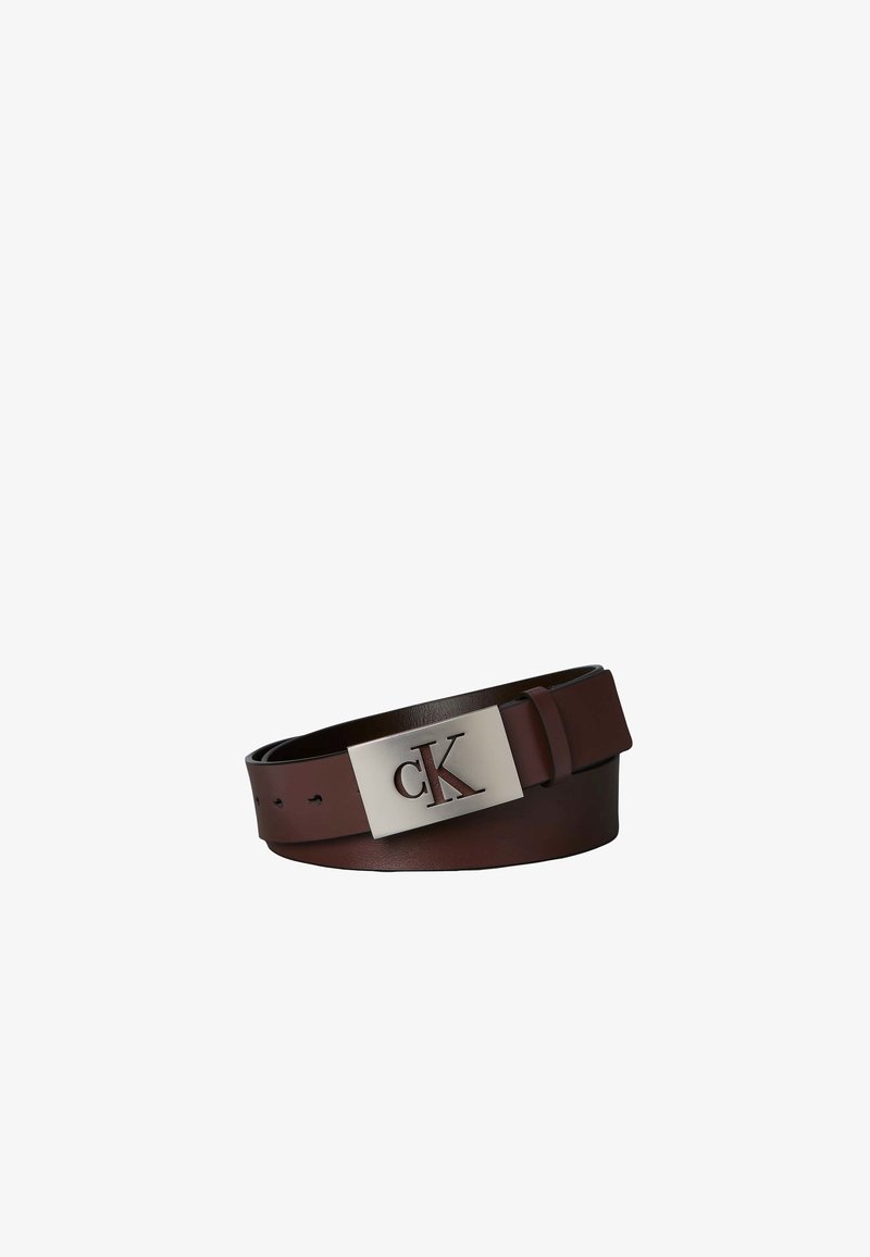 Ceinture en cuir marron roulée avec une boucle rectangulaire en argent présentant les lettres "cK" découpées.