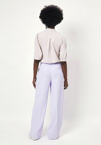 Lichtroze blouse met korte mouwen en gestructureerde schouders, gecombineerd met lila wijde broek met een trekkoord in de taille en achterzakken.