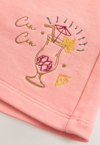Rosa Baumwollstoff mit gesticktem Cocktailglas, Eiswürfeln, einem Strohhalm, einem Regenschirm und einem Seestern. Umrandung in Gold und farbenfrohen Akzenten.