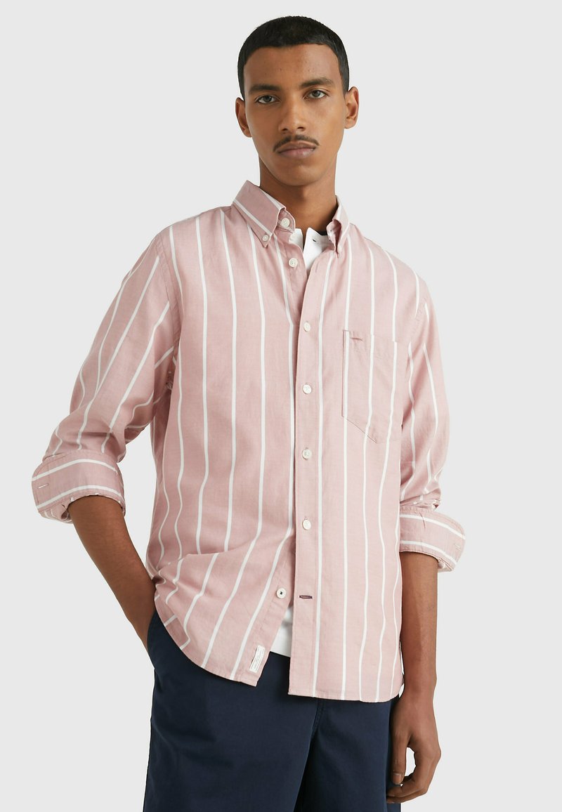 Camicia button-up rosa chiaro con strisce verticali bianche, taschino sul petto, maniche arrotolate e orlo curvo. Tessuto in cotone.