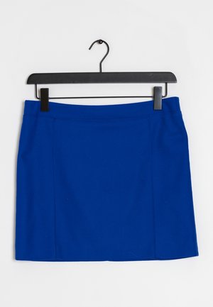 Falda azul hasta la rodilla colgada en una percha de plástico negra con clips sobre un fondo blanco.