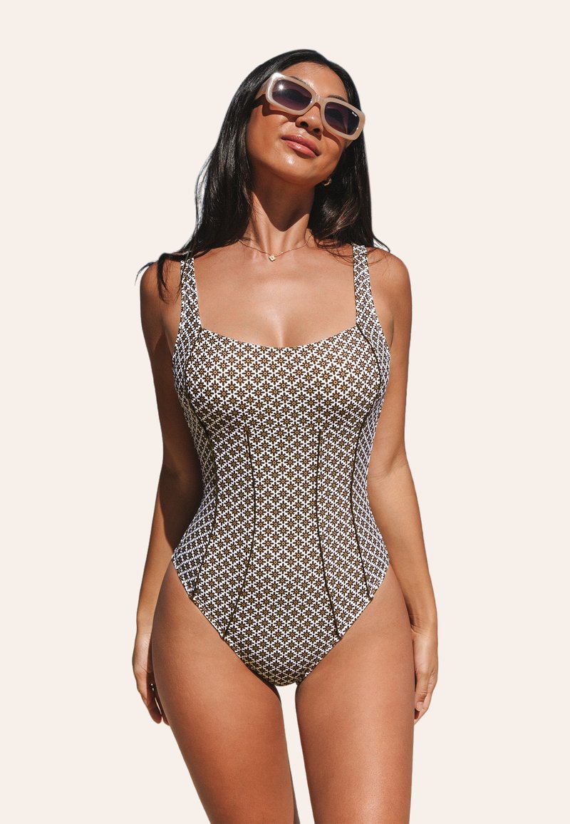 Traje de baño de una pieza con patrón marrón y blanco, escote cuadrado y tirantes anchos, que presenta un diseño ajustado y una textura suave.