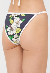 Close-up of a person wearing navy bikini bottoms with white hibiscus flower patterns and white trim.
