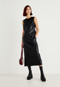 Schwarzes ledernes ärmelloses Oberteil, kombiniert mit einem passenden Midirock, der eine glatte Textur und ein minimalistisches Design aufweist, ergänzt durch klobige Plateaustiefel.