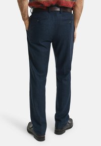 Marineblaues Woll-Hosen mit Fischgrätmuster, ausgestattet mit zwei Gesäßtaschen und einem Ledergürtel, kombiniert mit schwarzen Schuhen.