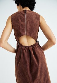 Bruine mouwloze jurk met een uitgesneden rug, voorzien van een ritssluiting en gathered taille detail. Gemaakt van textiel met een matte afwerking.