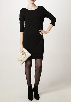 Robe noire ajustée avec un décolleté en scoop et des manches trois-quarts. Assortie à une pochette crème et des bottines noires. Tissu lisse.