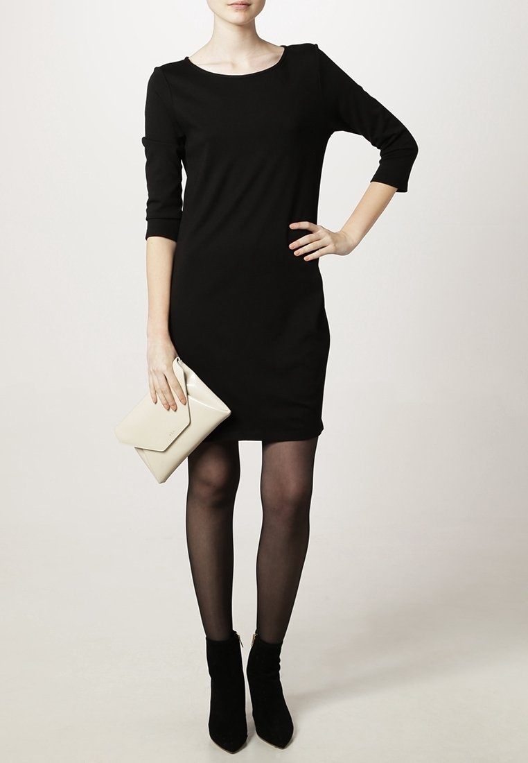 Robe noire ajustée avec un décolleté en scoop et des manches trois-quarts. Assortie à une pochette crème et des bottines noires. Tissu lisse.