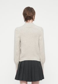 Suéter bege claro com bainha canelada e mangas bufantes, combinado com uma saia preta plissada. Textura suave com uma cor sólida.