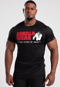 Black short-sleeve t-shirt with "GORILLA WEAR" and "UNITED STATES OF AMERICA" printed in red and white. Features a gorilla graphic.
