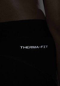 Tessuto atletico Therma-Fit nero con una texture liscia e dettagli riflettenti del logo. Design aderente con accenti di cucitura sui lati.