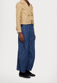 Beige cropped dubbele borstjasje met gouden knopen, gecombineerd met wijde blauwe denimsp pantalons met contrasterende witte stiksels.