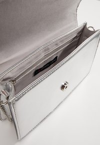 Srebrna metaliczna torebka o gładkiej fakturze, z zamykaną kieszonką wewnętrzną, metalowym zapięciem oraz łańcuszkowym paskiem.