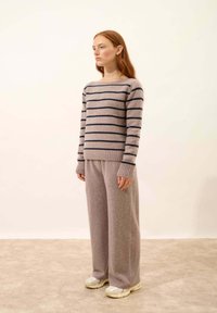 Jasnoszary sweter w paski o granatowych paskach, z prążkowanymi mankietami, w połączeniu z luźnymi, jasnoszarymi spodniami i beżowymi sneakersami. Proste, miękkie faktury.