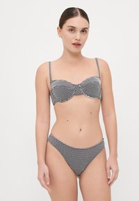 Bikini set v črno-beli karirasti vzorcu, ki vključuje rahlo podložen top s kovinskimi žicami, nastavljivimi naramnicami in ujemajočimi se nizkimi bikini hlačkami.