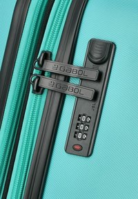 Maleta rígida turquesa con superficie texturizada, doble cremallera negra y una cerradura combinada que muestra tres diales numéricos.