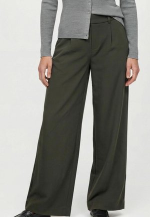 Femme portant un pantalon large vert foncé associé à un cardigan gris côtelé boutonné et des chaussures noires.