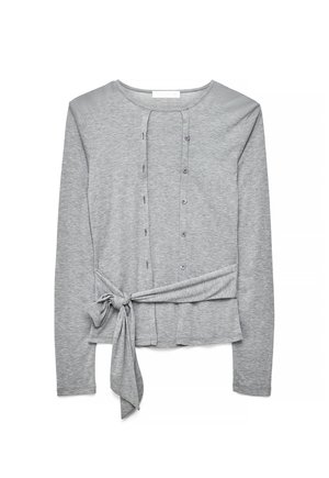 Šviesiai pilkas megztinis ilgomis rankovėmis su priekiniais mygtukais ir šonine rišimo kilpa, pagamintas iš minkštos, lengvos medžiagos.