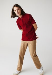 Röd polo skjorta med krage, korta ärmar och knappdetalj. Matchad med khakifärgade chinos och vita sneakers för en avslappnad look.