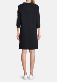 Czarna sukienka do kolan z rękawami 3/4, z okrągłym dekoltem i zamkiem błyskawicznym z tyłu. Na rękawie napis "SOBIE".