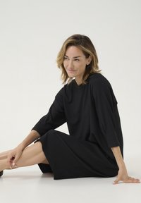Robe noire à la texture, à coupe ample, avec des manches trois-quarts et un col rond, tombant juste au-dessus du genou. Tissu lisse.