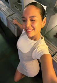Strapless gestreepte jurk over een witte t-shirt. Gladde stof, aansluitend ontwerp, model staat naast een plank met vinylplaten. Heldere verlichting.