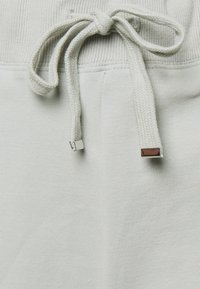 Pantalons de jogging gris clair avec une taille côtelée, dotés d'un cordon de serrage avec des embouts métalliques et d'une texture lisse et douce.