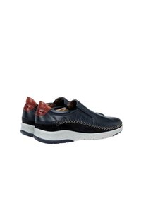 Zapatos de cuero tipo slip-on con una parte superior azul marino y acentos rojos, detalles de costura y una suela blanca con un acabado texturizado.