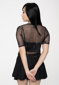 Sheer black top with a marble pattern and short sleeves, paired with a black skirt. The fabric has a slight sheen.