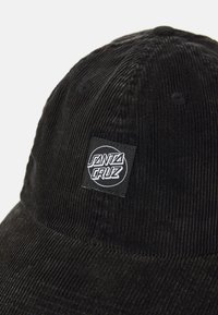 Capa de cabedal preta com aba reta, apresentando um patch de logo quadrado que diz "Santa Cruz" em branco. Tecido texturizado com sulcos.