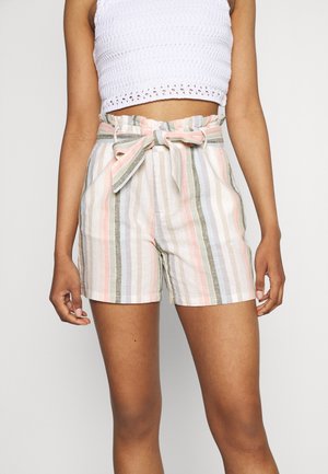 Mujer con pantalones cortos de cintura alta a rayas en tonos pastel con cinturón anudado y top corto texturizado blanco, de pie frente a un fondo liso.